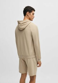 Sudadera beige hecha de un tejido suave con un bolsillo tipo canguro, que cuenta con una capucha con cuerda y puños acanalados, acompañada de pantalones cortos a juego.