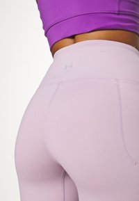 Světle fialové sportovní legíny s plochými švy, vysokým pasem a malým logem na zadní straně, které ukazují hladkou, elastickou tkaninu.
