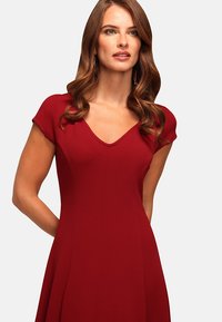 Red dress with short cap sleeves, V-neckline, fitted bodice, and flared skirt. Fabric appears smooth with a slight texture.