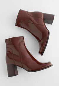 Bottines en cuir verni bordeaux avec un bout carré et un talon bloc. Texture lisse avec de discrets détails de coutures sur les côtés.