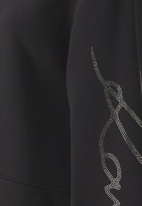 Zwarte sweatshirt met een textuur en glanzende zilveren versiering in een vloeiende abstracte patroon langs de mouw. Zachte, flexibele stof.