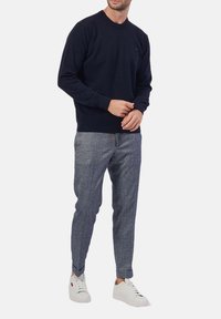 Maglione a maglia blu marino con collo rotondo abbinato a pantaloni grigi chiari a fantasia e sneakers bianche basse. Insieme semplice e casual.