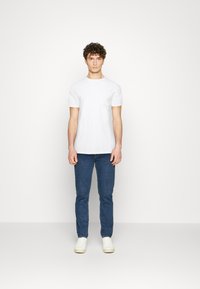 Hvit t-skjorte med korte ermer, rund hals og brystlomme, kombinert med mørkeblå jeans og hvite joggesko. Enkel, klassisk design.
