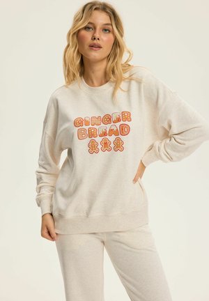 Świetny beżowy sweatshirt o luźnym kroju i okrągłym dekolcie. Posiada kolorową grafikę "GINGERBREAD" w odcieniach czerwieni i pomarańczy, w zestawie z dopasowanymi spodniami.