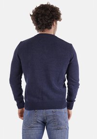 Maglione lavorato a maglia blu navy con scollo rotondo, tessuto strutturato e polsini e orlo a coste, indossato su jeans blu chiaro.
