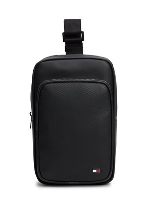 Μαύρη ορθογώνια τσάντα crossbody με διάτρητη μπροστινή τσέπη, φερμουάρ, ρυθμιζόμενο λουράκι και μικρό ορθογώνιο λογότυπο σε κόκκινο, άσπρο και μπλε χρώμα.