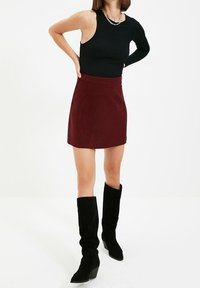 Černý žebrovaný top bez rukávů v kombinaci s burgundskou mini sukní. Modelka má na sobě černé semišové kozačky po kolena s blokovým podpatkem. Jemný kovový detail na náhrdelníku.