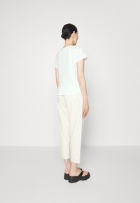 Gaišs piparmētru krāsas īsu piedurkņu T-krekls, gluda auduma, nedaudz izliekta apakšmala. Apvienots ar bēšām, šaurām biksēm un melnām platformām.