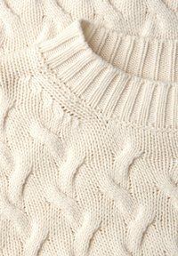 Biały dzianinowy sweter z wzorem warkoczowym i prążkowanym dekoltem. Struktura jest gruba i przytulna, z wypukłymi detalami ściegów.