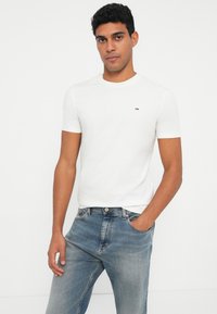 Λευκό κοντομάνικο μπλουζάκι από βαμβάκι, με μικρό έγχρωμο λογότυπο στο στήθος, σε συνδυασμό με τζιν παντελόνι ανοιχτού χρώματος.