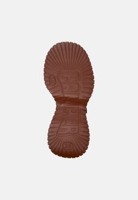 Semelle de chaussure en caoutchouc brun avec un motif nervuré, portant l'empreinte "CAMPER" et la taille "38" notée. Texture lisse et bords arrondis.