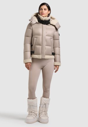 Beige pufferjacka med en shearlingfoder i huvan och kragen, framfickor, svarta detaljer, tillsammans med matchande leggings och vita snöskor.
