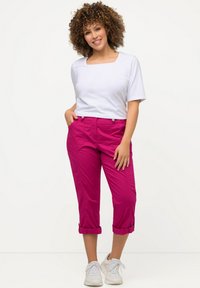 Top blanc à encolure carrée associé à un pantalon rose cropped et retroussé, doté de deux poches avant et de bouton-pression en argent. Porté avec des baskets blanches.