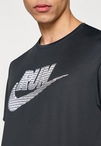 Čierne bavlnené tričko s okrúhlym výstrihom, s textúrovanou bielou grafikou s nápisom "RUN" v dynamickom štýle na prednej strane.