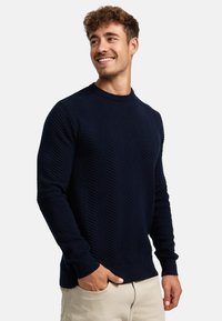 Marineblå genser med en teksturert herringbone-mønstret, rund utringning og lange ermer. Materialet ser ut til å være strikket med ribbestrikkede mansjetter og hem.