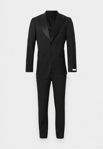 Čierny smokingový oblek s atlasovým špičkovým klopou, zapínaním na dva gombíky, jedným náprsným vreckom a úzkymi nohavicami s prelisovanými záhybmi.