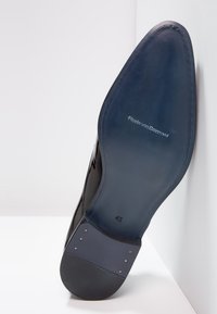 Semelle de chaussure en cuir noir avec une surface lisse, de forme rectangulaire et avec un bout arrondi, marquée du chiffre "41" et de détails de logo.