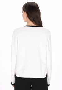 Witte trui met zwarte accenten bij de kraag en zoom, voorzien van lange mouwen en een relaxte pasvorm. Zachte, gladde textuur.