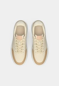 Baskets beiges avec des accents perforés, des superpositions contrastantes en tan et des lacets crème. Dotées d'un bout rond et d'une semelle en caoutchouc blanche.