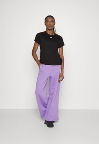 Svart t-skjorte med kort erme og en liten hvit logo, parret med løstsittende lavendel joggebukser og svarte treningssko.