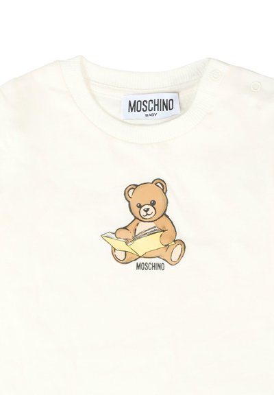 Chemise en coton blanc pour bébé avec une illustration d'un ours en peluche marron lisant un livre jaune, le tout surmonté du mot "Moschino" imprimé en dessous de la conception.