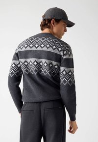 Un pull en tricot gris foncé avec un motif géométrique blanc sur les épaules. Il présente des poignets ajustés et un col rond.