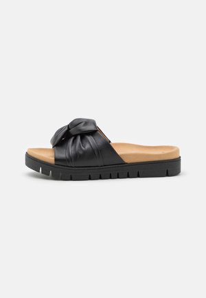 Sandale slide noire avec semelle intérieure beige rembourrée, bride en cuir nouée et semelle épaisse noire texturée, vue de côté sur fond blanc.