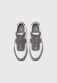 White and grey sneakers with a smooth upper, textured grey suede accents, round laces, and a black logo on the tongue.
