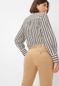 Chemise rayée à manches longues noire et blanche, associée à un pantalon beige. La chemise présente un col classique et des poignets boutonnés. Le pantalon comporte des poches arrière.