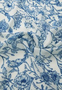 Bjela tkanina s detaljnim plavim cvjetnim uzorkom, s raznim dizajnom cvijeća i lišća, stvarajući mekan i teksturiran izgled.