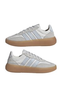 Zapatillas grises y blancas con parte superior de ante y cuero, tres franjas azul claro, punta redonda y suela de goma marrón clara.