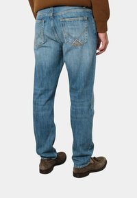 Jeans in denim azzurro chiaro con taglio dritto, dotati di due tasche posteriori con un motivo di cucitura a diamante. Indossati con scarpe marroni.