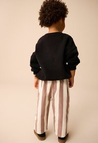 Zwarte sweatshirt met lange mouwen, gecombineerd met brede gestreepte broeken in licht crème en zacht roze. Schoeisel is donkerbruin.