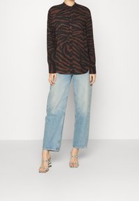 Brown and black zebra-striped shirt with buttons, paired with light blue wide-legged jeans and black and white striped high-heeled sandals.