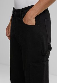Pantaloni cargo negri, cu o croială lejeră, având buzunare laterale și un tiv cu închidere tip buton. Realizați dintr-un material rezistent, cu o textură simplă.