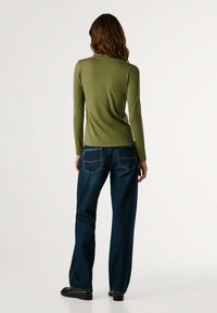 Olivgrünes langärmliges Oberteil kombiniert mit blauen weit geschnittenen Jeans. Das Oberteil hat einen runden Ausschnitt, während die Jeans über Gesäßtaschen verfügen.