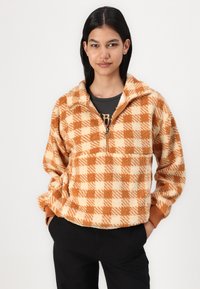 Fleece puloveris su patikrinu raštu oranžiniais ir cream spalvomis, pusiau užtrauktuku ir megztomis rankovėmis. Minkšta tekstūra ir laisvas siluetas.