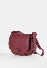 Bordeauxroter Ledersattel mit Klappverschluss, verstellbarem Riemen und geschwungenem Design. Glatte Textur mit dezenten Nahtdetails.