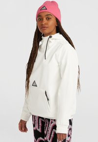 Witte pullover jas met een capuchon, een voorzak en zwarte accenten. Gekocht met zwarte broeken met een roze en witte abstracte print, en een roze beanie.
