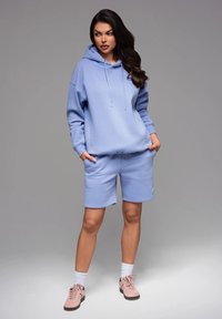 Ensemble en sweat à capuche bleu clair et short en tissu doux, présentant une coupe décontractée, des cordons de serrage et un accent logo. Associé à des baskets rose clair.