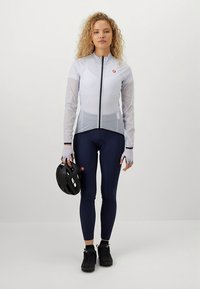 Cykeltøj med en lysegrå langærmet trøje med lynlås og mesh-detaljer, kombineret med marineblå leggings og en sort hjelm.