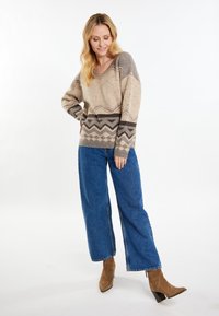 Pulover bej tricotat, cu decolteu în V, prezentând modele geometrice maronii la tiv. Asortat cu blugi largi albaștri și cizme ancle din suede maro.