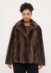 Brązowy płaszcz z sztucznego futra z szerokim kołnierzem, luźnym krojem i miękką fakturą. Posiada zapięcie na guziki oraz swobodny krój.