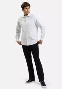 Biała, w paski koszula z długim rękawem, slim fit, noszona z czarnymi spodniami i ciemnymi sneakersami. Prosty design, bez widocznych wzorów czy akcentów.