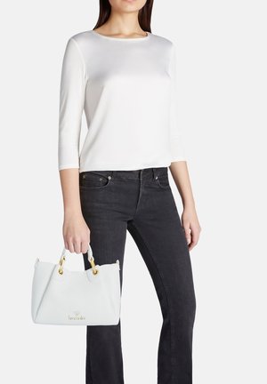 Top bianco a maniche corte abbinato a jeans neri. La persona tiene una borsa azzurro chiaro con hardware dorato e una finitura testurizzata.