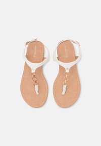 Sandales en simili cuir blanc avec une semelle matelassée couleur tan, ornées d'accents en chaîne dorée et de brides de cheville réglables. Design plat, style ouvert à l'avant.