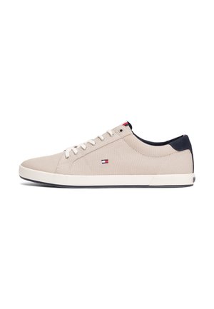 Basket basse beige avec lacets blancs, accent bleu marine au talon et petit logo rouge, blanc et bleu sur le côté, montrée de profil gauche.