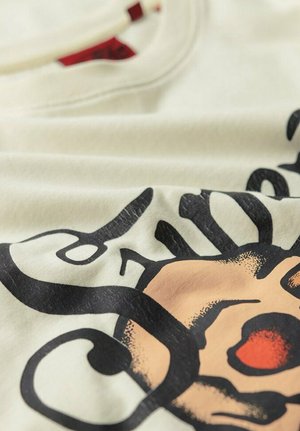 Kræmfarvet bomulds t-shirt med et stort sort grafisk design og orange detaljer. Glat tekstur med rund halsudskæring.