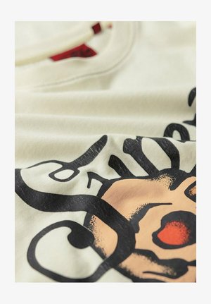 Crème-kleurige katoenen t-shirt met een grote zwarte grafische afbeelding en oranje accenten. Glad textuur met een ronde halslijn.