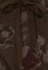 Brun tyg med blommönster i nyanser av grått och vinrött, med ett matchande tygband i midjan. Mjuk textur och lagerdesign.